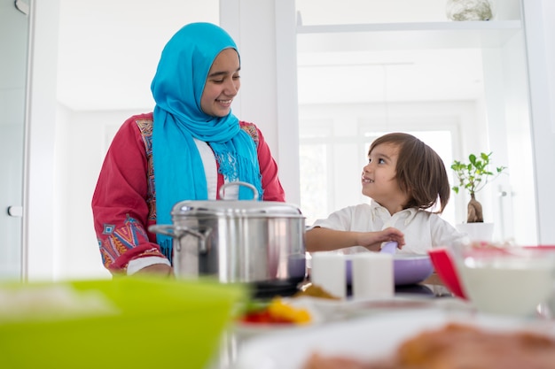 Mulher muçulmana tradicional com filho pequeno na moderna cozinha branca