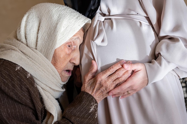 Mulher muçulmana velha se sentindo entusiasmada com seu novo neto toca na barriga de sua filha para sentir os movimentos do feto