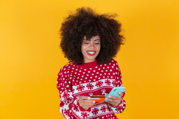 mulher muito afro-americana, compras de natal com smartphone e cartão de crédito, fundo amarelo,