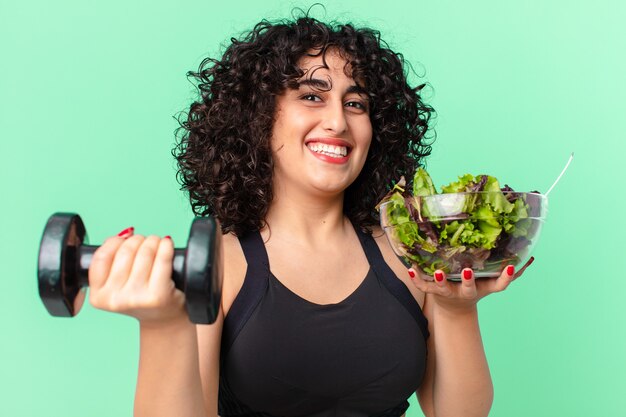 Mulher muito árabe com um haltere e uma salada. conceito de fitness