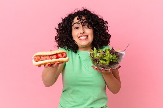 Mulher muito árabe segurando uma salada e um cachorro-quente. conceito de dieta