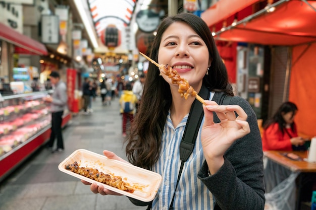 Mulher muito asiática desfrutando de comida de rua. uma espécie de cozinha japonesa yakitori sorrindo agradavelmente.