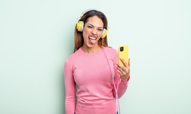 Mulher muito hispânica com atitude alegre e rebelde brincando e enfiando a língua para fora o conceito de smartphone e fones de ouvido