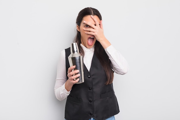 Mulher muito hispânica parecendo chocada, assustada ou aterrorizada, cobrindo o rosto com a mão. conceito de coquetel de barman