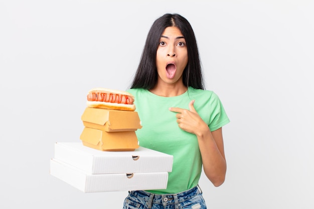 Mulher muito hispânica parecendo chocada e surpresa com a boca aberta, apontando para si mesma e segurando as caixas de fast food