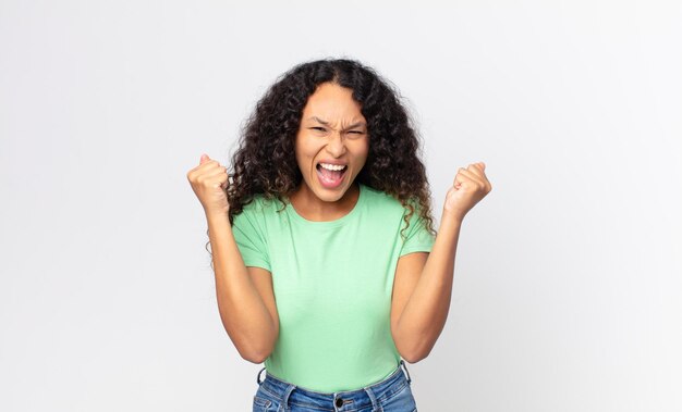 Mulher muito hispânica parecendo extremamente feliz e surpresa comemorando o sucesso gritando e pulando