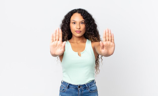 Mulher muito hispânica parecendo séria, infeliz, irritada e descontente, proibindo a entrada ou dizendo pare com as duas palmas abertas