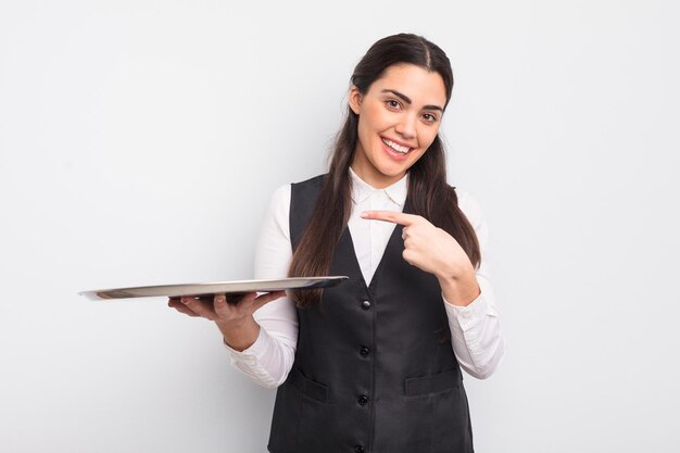 Mulher muito hispânica sorrindo alegremente se sentindo feliz e apontando para o garçom do lado com o conceito de bandeja