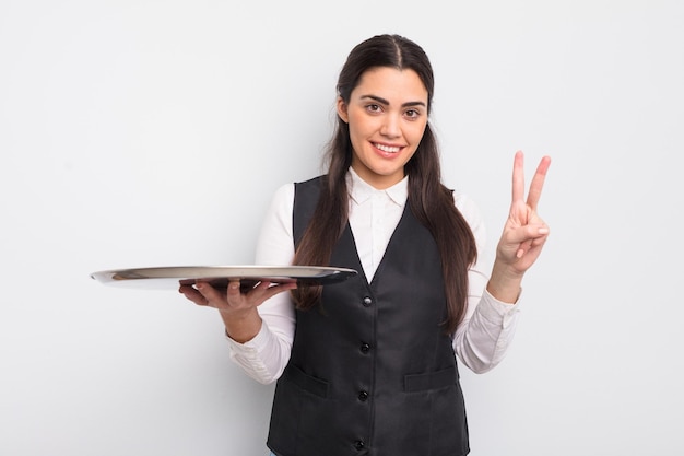 Mulher muito hispânica sorrindo e parecendo amigável mostrando o garçom número dois com o conceito de bandeja