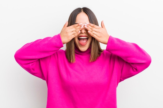 Mulher muito hispânica sorrindo e se sentindo feliz cobrindo os olhos com as duas mãos e esperando uma surpresa inacreditável