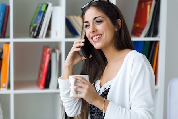 Mulher muito jovem que usa seu celular no escritório.