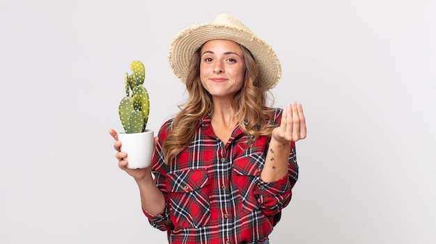 Mulher muito magra fazendo capice ou gesto de dinheiro, dizendo para você pagar segurando um cacto. conceito de fazendeiro