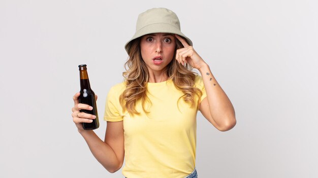 Mulher muito magra parecendo surpresa, percebendo um novo pensamento, ideia ou conceito e segurando uma cerveja. conceito de verão