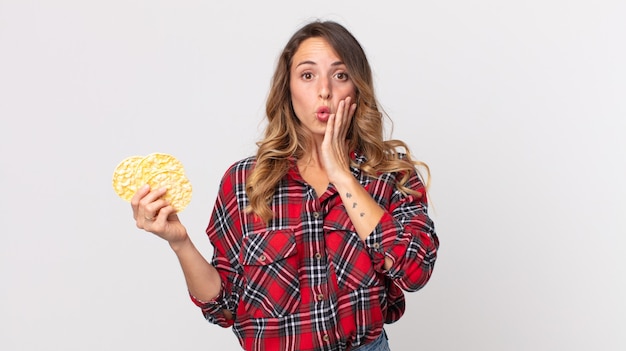 mulher muito magra se sentindo chocada e assustada segurando um bolo de arroz diet