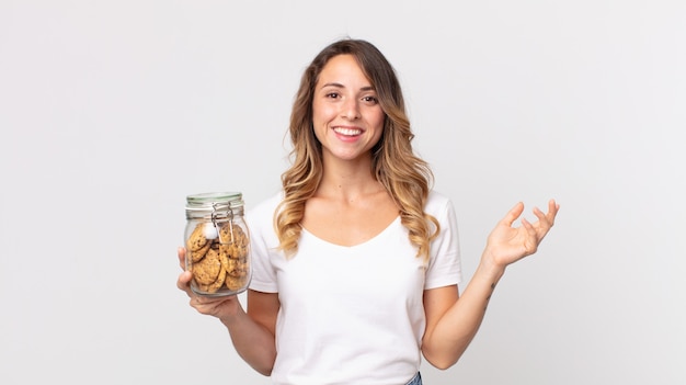 Mulher muito magra se sentindo feliz, surpresa ao perceber uma solução ou ideia e segurando uma garrafa de vidro de biscoitos