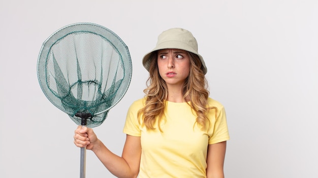 Mulher muito magra se sentindo triste, chateada ou com raiva e olhando para o lado com um chapéu e segurando uma rede de pesca