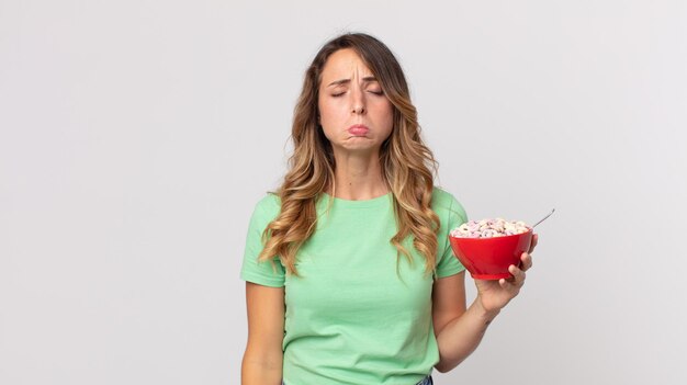 Mulher muito magra se sentindo triste e chorosa com um olhar infeliz e chorando e segurando uma tigela de café da manhã