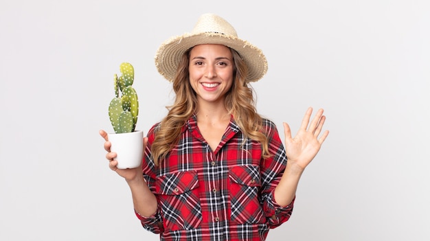 Mulher muito magra, sorrindo alegremente, acenando com a mão, dando as boas-vindas e cumprimentando você segurando um cacto. conceito de fazendeiro