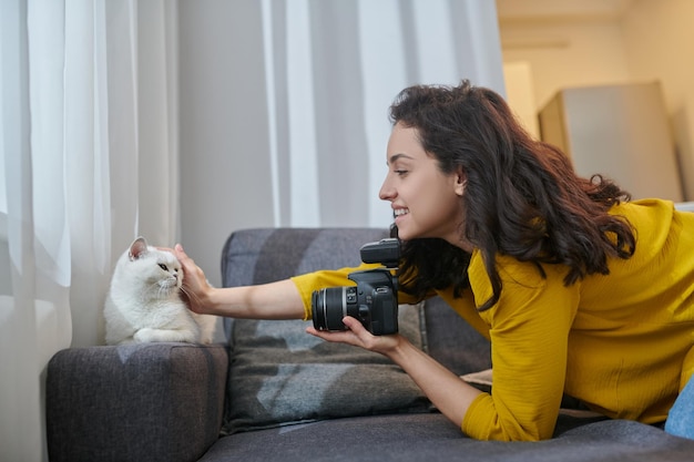 Mulher muito morena com câmera acariciando seu gato branco