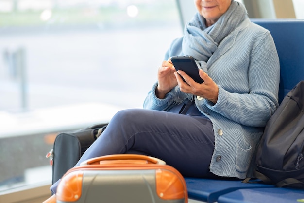 Mulher muito sênior usando conexão de celular para enviar mensagens e conversar Pessoas do conceito de viajante com mochila e malas Mulher idosa usa celular no aeroporto