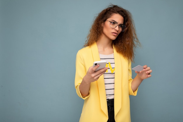 Mulher muito triste e muito chateada, vestindo roupas elegantes do dia a dia, isoladas na parede de fundo, segurando e