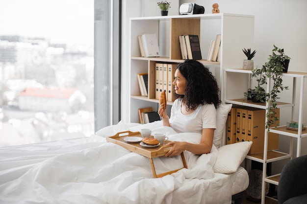 Mulher multiétnica tomando café da manhã na cama confortável