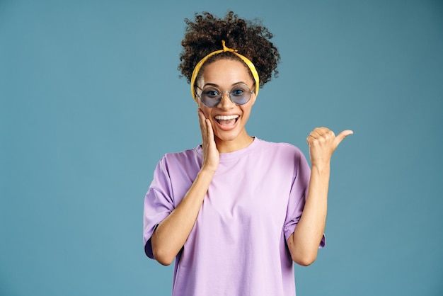 Mulher multirracial positiva apontando o dedo para longe enquanto presta atenção no espaço vazio para propaganda