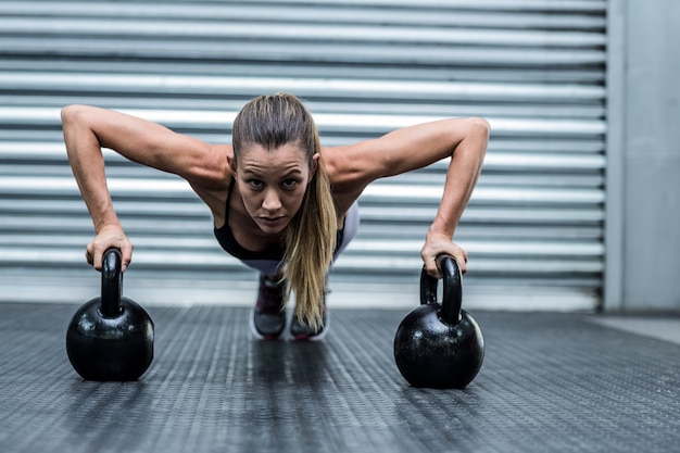 Mulher muscular fazendo flexões com kettlebells