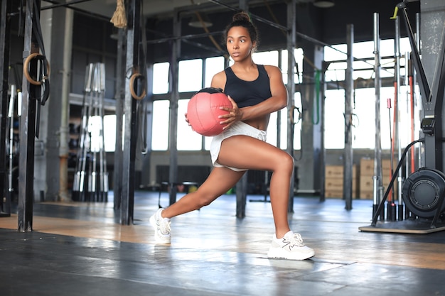 Mulher musculosa e apta, exercitando-se com a bola de medicina no ginásio.