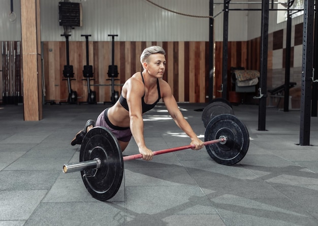 Mulher musculosa treinando mishtsi press com barra no ginásio moderno