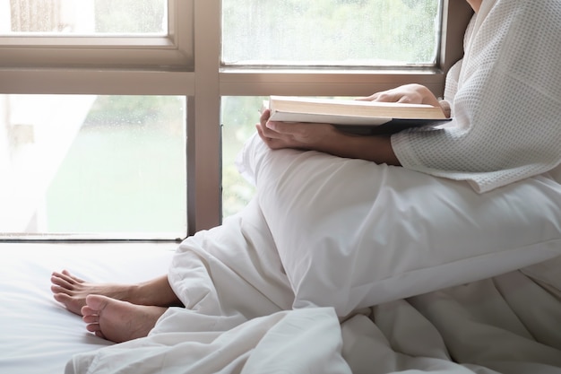 Mulher na cama e lendo um livro.