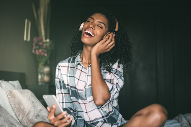 Mulher na cama ouvindo música com fones de ouvido e smartphone