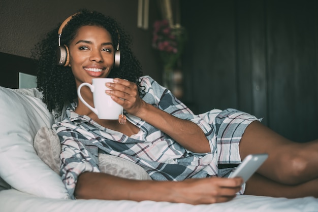 Mulher na cama ouvindo música com fones de ouvido e smartphone