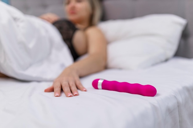 Mulher na cama sob lençóis segurando o vibrador na mão