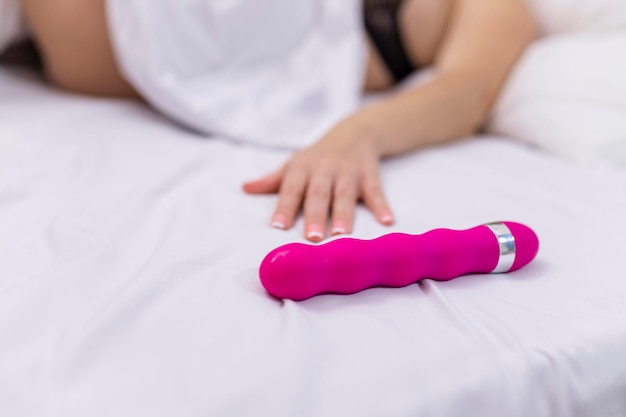 Mulher na cama sob lençóis segurando o vibrador na mão