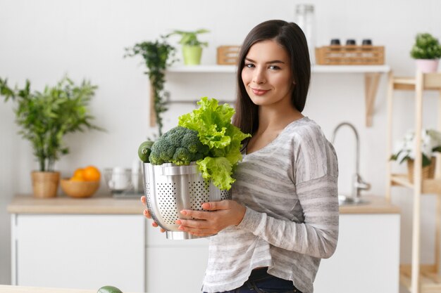 Mulher na cozinha em casa com vegetais verdes cozinhando. Helthy casa comida dieta vitaminas jovem e bela fêmea. Tiro do estúdio.