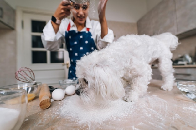 Mulher na cozinha peneira farinha junto com um cachorro