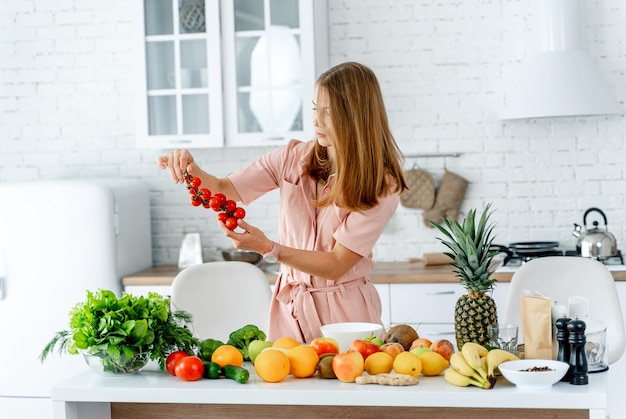 Mulher na cozinha pronta para preparar a refeição com legumes e frutas mulher está olhando tomates nas mãos fundo da cozinha comida saudável vegans vegeterian