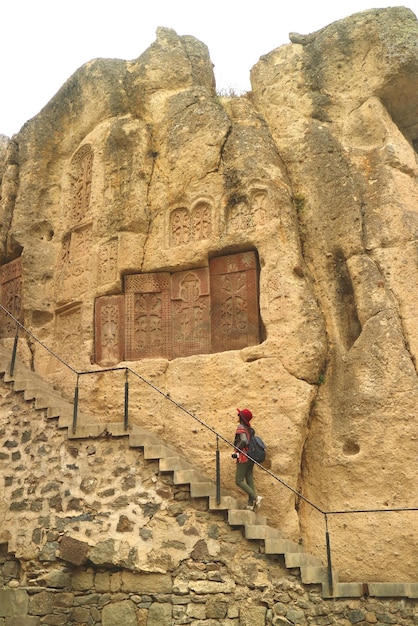 Mulher na escada com pedras Khachkar ou Cross na parede do penhasco no mosteiro de Geghard Armênia