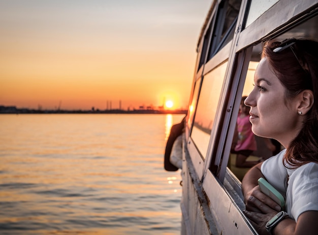 Mulher na janela do barco de recreio olhando o belo pôr do sol