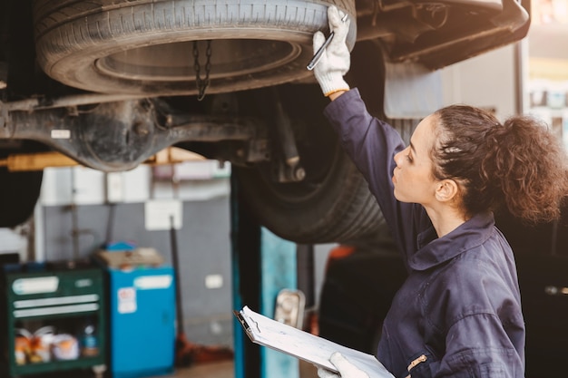 Mulher na lista de verificação de manutenção do trabalhador de garagem no centro de serviço automotivo, Mulher no mecânico de automóveis, técnico de automóveis, verificar e consertar o carro do cliente, inspecionando o carro sob o capô