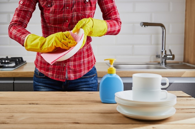 Foto mulher na luva protetora amarela com pratos, pratos e pano, mesa de madeira, fundo de cozinha. conceito de lavagem e limpeza.