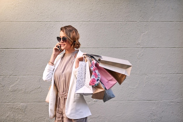 Mulher na moda falando ao telefone depois de uma maratona de compras na cidade Jovem mulher elegante, aproveitando seu tempo livre com terapia de varejo no centro, sorrindo e feliz com uma venda e compra