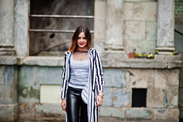 Mulher na moda parece com calças de couro de paletó listrado preto e branco posando na velha rua Conceito de garota da moda