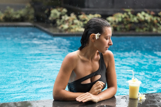 Mulher na piscina com suco de frutas.