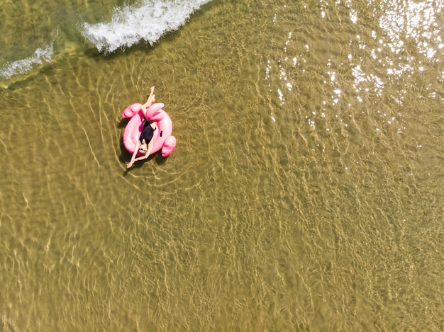 Mulher na piscina do flamingo flutua no mar, vista aérea do drone