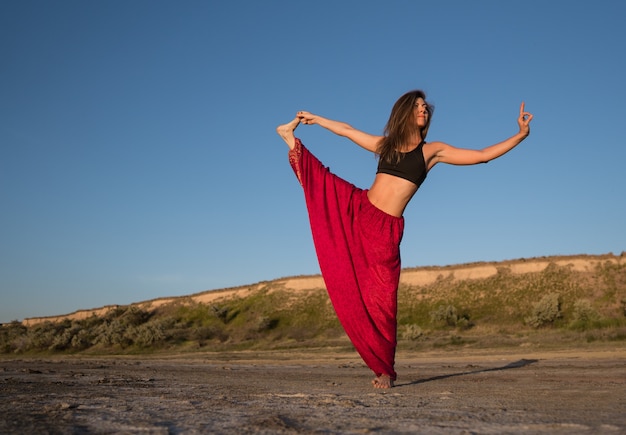 Mulher na praia ao pôr do sol fazendo ioga asana. Treino de alongamento natural matinal de aquecimento