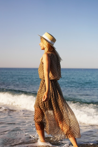 Mulher na praia com um vestido marrom e um chapéu de palha de férias na praia