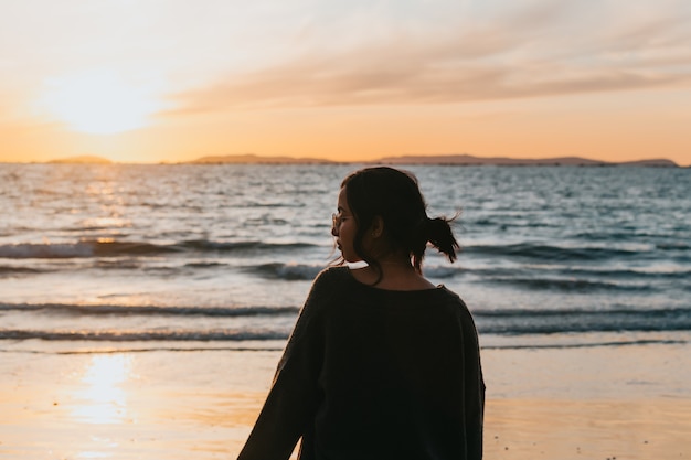 Mulher na praia olhando um pôr do sol colorido em um dia ensolarado