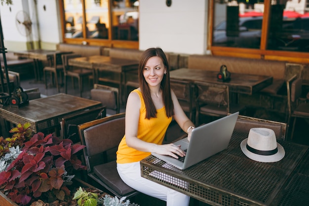 Mulher na rua ao ar livre, café, café, sentada à mesa, trabalhando em um moderno laptop, relaxando no restaurante durante o tempo livre